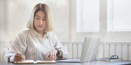 Young professional businesswoman working on her project and writing on notebook in her comfortable office roomの写真素材