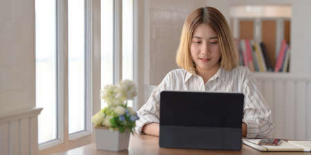 Young beautiful businesswoman working on her project while typing on tablet in comfortable workplaceの写真素材