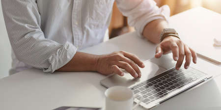 Close-up view of professional businessman typing on laptop computer while working on his project in modern officeの写真素材