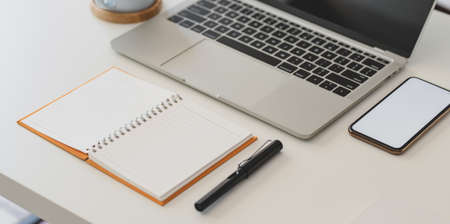 Cropped shot of comfortable workplace with open notebook, laptop computer and smartphone on white wooden tableの写真素材