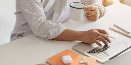 Cropped shot of professional businessman typing on laptop computer while drinking a cup of coffeeの写真素材