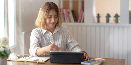 Professional young female designer working on her project with digital tablet in comfortable workspaceの写真素材