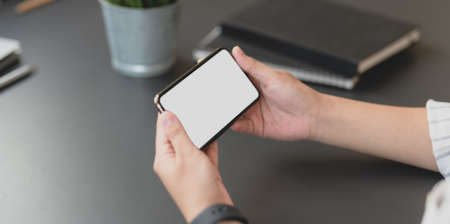 Cropped shot of professional businesswoman holding horizontal blank screen smartphone in his office roomの写真素材
