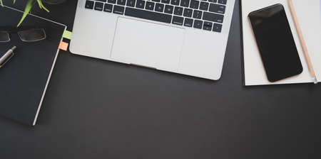 Top view of dark modern workspace with laptop computer and office supplies on black table backgroundの写真素材
