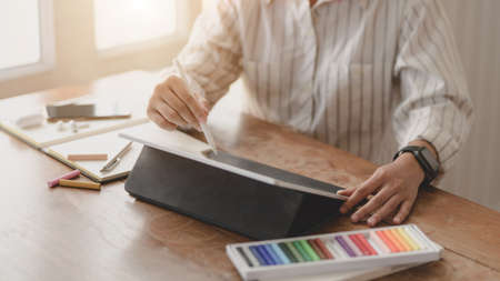 Cropped shot of young professional designer drawing on her project with blank screen tablet in comfortable workspaceの写真素材