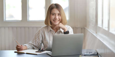 Portrait of young professional businesswoman working on her project with laptop computer and smiling to the cameraの写真素材