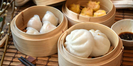 Chinese steamed dumpling and steamed pork bun in a bamboo steamer with chopstick on wooden tableの写真素材