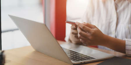 Cropped shot of young businesswoman holding smartphone while working on laptop computer in comfortable workplaceの写真素材