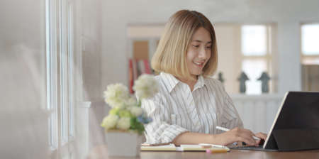 Portrait of young female professional designer working on her project with  tablet in her comfortable workplaceの写真素材