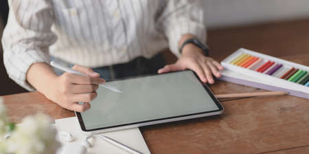 Cropped shot of young professional female designer working on blank screen tablet in her workspace with office suppliesの写真素材