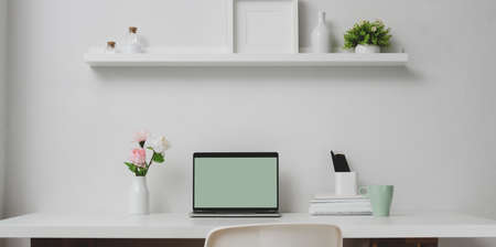 Minimal workspace with open laptop computer and decorations on the shelf, white table and white wall backgroundの写真素材