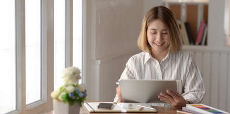 Young female designer working on her project with digital tablet in comfortable workspaceの写真素材