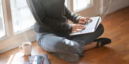 Cropped shot of young female freelancer typing on laptop computer while sitting next to the windows with a cup of hot cocoaの写真素材