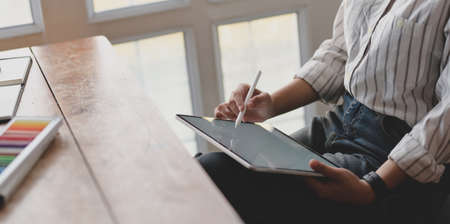 Cropped shot of young professional female designer working on blank screen tablet in her workspace with office suppliesの写真素材