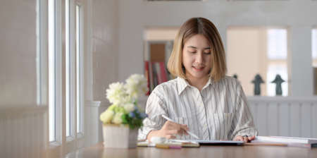 Beautiful female designer working on blank screen tablet in her workspace with office suppliesの写真素材