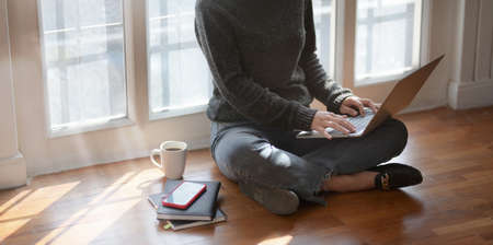 Close-up view of young female freelancer typing on laptop computer while sitting next to the windows with a cup of hot cocoaの写真素材