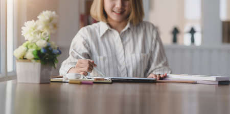 Beautiful female designer working on blank screen tablet in her workspace with office suppliesの写真素材