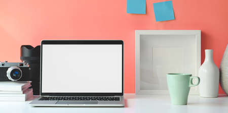 Minimal workspace with open blank screen laptop computer with blank poster frameの写真素材