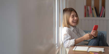 Young beautiful female designer looking at smartphone and sitting on the chair in her comfortable workspaceの写真素材