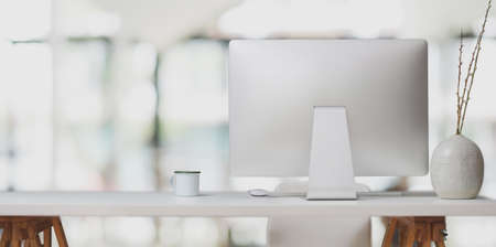 Desktop computer on white table and coffee cup in modern office room with blurred backgroundの写真素材