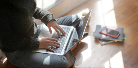 Close-up view of young female freelancer working on her project with laptop computer while sitting near the windowsの写真素材