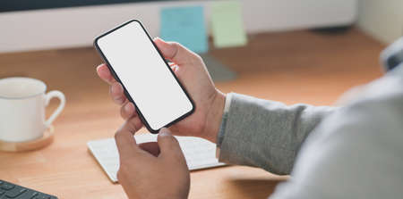 Cropped shot of young businessman holding blank screen smartphone while working on his project in his office roomの写真素材