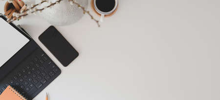 Top view of modern workspace with digital tablet, keyboard, smartphone and coffee cup on white table