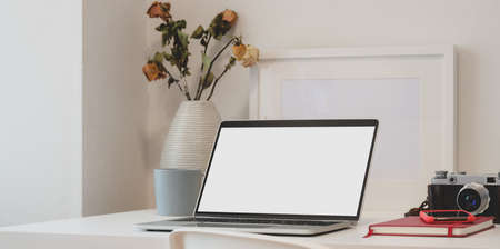 Contemporary workspace with laptop computer, camera, office supplies and dry roses vase on white tableの写真素材