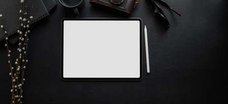 Top view of blank screen digital tablet on blank desk in dark luxury workspace with office supplies の写真素材