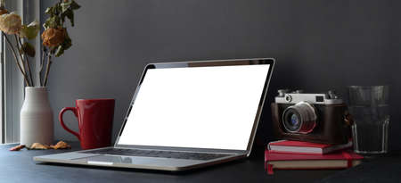 Dark trendy workspace with laptop computer and camera on black desk and dark grey wall with office supplies の写真素材