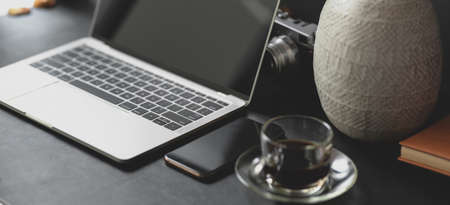 Cropped shot of dark modern workspace with laptop computer, smartphone and coffee cup の写真素材