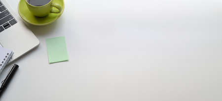 Top view of modern workplace with laptop computer and green coffee cup on white table and sticky noteの写真素材