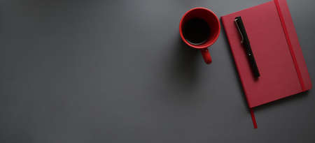Top view of dark modern workplace with red notebook and red coffee cup on dark grey desk backgroundの写真素材