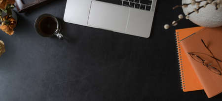 Overhead shot of dark modern workspace with laptop computer, orange notebook with office supplies on black leather desk の写真素材