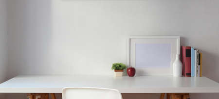Minimal workspace with copy space and mock up frame with books on white table and white wall background の写真素材