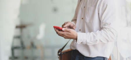 Cropped shot of young professional businessman holding smartphone in his office room の写真素材