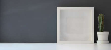 Mock up frame with cactus in pot in modern workspace on white table and dark grey wall backgroundの写真素材
