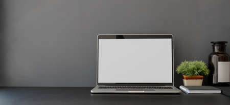 Open blank screen laptop computer in dark trendy workplace with copy space and decorations の写真素材