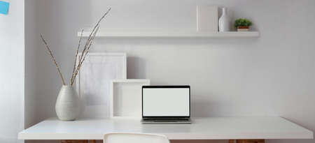 Loft style workplace with open blank screen laptop computer and mock up frame on white table 
