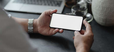 Close-up view of businessman holding blank screen smartphone in his modern office room while working on his project の写真素材