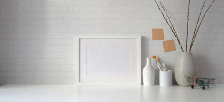 Minimal workspace with copy space and mock up frame with books on white table and white wall background の写真素材