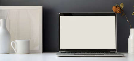 Minimal office room with open blank screen laptop computer with mock up frame decorations の写真素材
