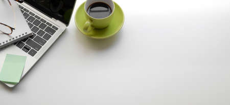 Overhead shot of modern workplace with laptop computer and green coffee cup on white table and copy spaceの写真素材