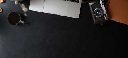 Overhead shot of dark modern workspace with laptop computer, orange notebook with office supplies on black leather desk の写真素材