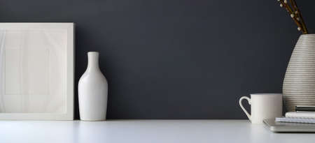 Modern workspace with mock up frame and ceramic vase on white table and grey wall background with copy space の写真素材