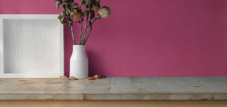 Modern workspace with mock up frame, dry roses vase and copy space on wooden table and pink wall background の写真素材