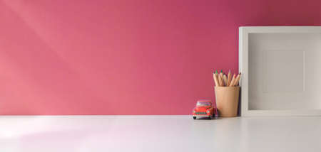 Modern workspace with mock up frame and copy space on white wooden table and pink wall background の写真素材