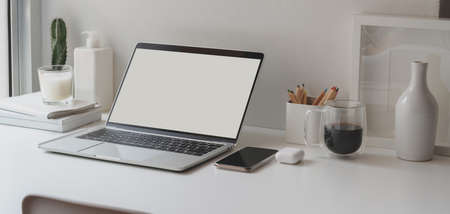 Minimal workspace with open blank screen laptop computer and office supplies on white wooden tableの写真素材