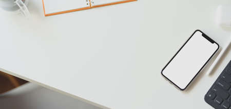 Overhead shot of minimal workspace with mock up smartphone with office supplies on white wooden...