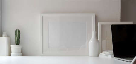 Minimal office room with mock up frame and decorations on white wooden table and white wall backgroundの写真素材